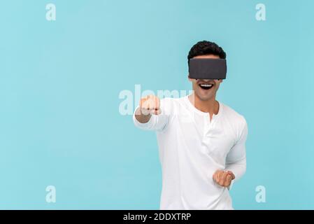 Excited Asian man wearing virtual reality or VR glasses and punching while playing  3D simulation video game on light blue background with copy space Stock Photo