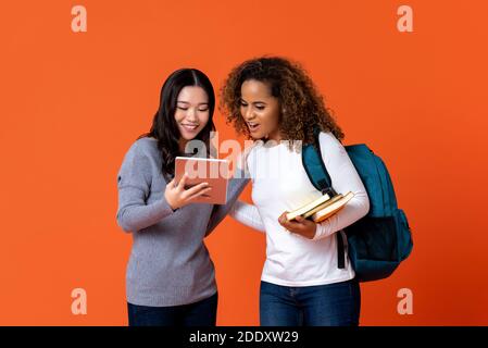 Interracial university students as friends looking at tablet computer isolated on colurful orange background Stock Photo