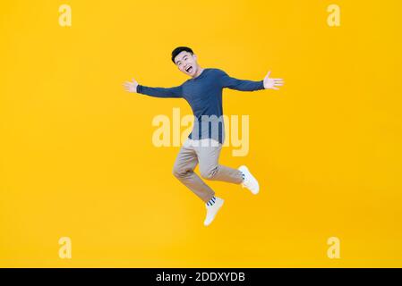 Full body of young dynamic handsome Asian man smiling and jumping with arms outstretched  isolated on yellow background Stock Photo