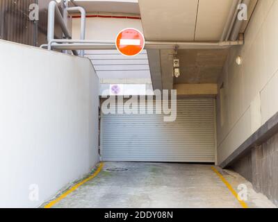 Entrance to the underground parking of the building with a closed roller shutter and a red prohibiting sign hanging above it Stock Photo