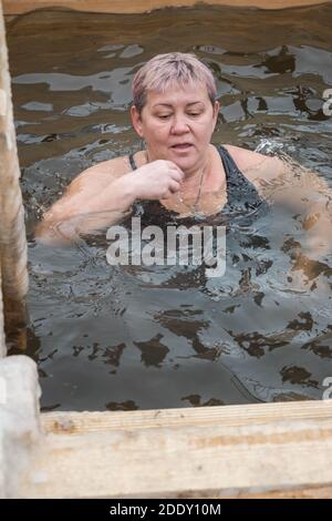 Nizhny Tagil, Russia - January 19, 2020: Elderly woman bathes into cold water of ice-hole on Epiphany day. Traditional ice swimming in Orthodox church Stock Photo