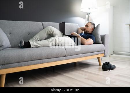 Man Lying In Sofa At Home And Using Laptop Stock Photo