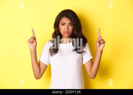 Portrait of upset and disappointed teenage african-american girl, complaining and frowning, pointing fingers up at something upsetting, standing over Stock Photo