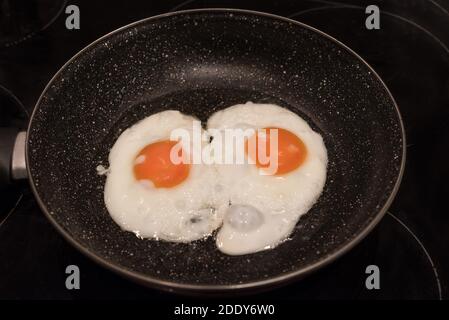 Chicken eggs in Frying Pan. Fried eggs in a cast iron pan close-up, breakfast, omelet, two eggs with yellow yolks are fried on the stove. Stock Photo