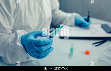 Scientist hand holding a syringe with virus vaccine in the laboratory. Selective focus on vaccine in the foreground Stock Photo