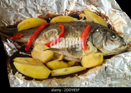 Fish stewed with potatoes and red pepper in foil. Hot dinner on table close-up Stock Photo