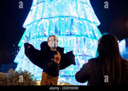 A kid poses for a photo next to Christmas tree at Puerta del Sol, Madrid's central square.Madrid officially starts the Christmas season by turning on 10.8 million LED lights throughout the capital. In total, there are more than 210 illuminated streets distributed throughout the 21 districts of the city of Madrid. The Community of Madrid proposed to the Spanish Ministry of Health a plan for Christmas, in which family and social gatherings are with a maximum of 10 people from three different groups of partners. Also on December 24, 25, 31 and January 1 and 6, a curfew at 1.30 am. Stock Photo