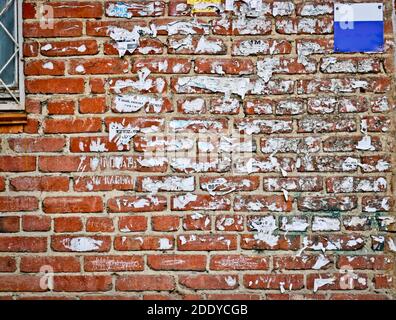 Red brick wall in original color with scraps of old pasted ads. Vintage background for creative design. The old wall. Stock Photo
