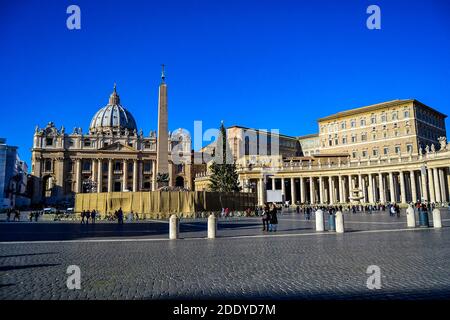 Main facade and dome of St. Peter's Basilica seen from St. Peter's Square. Tourists walking around the square during sunny day.