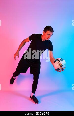 Football player in sportswear, a man playing with his feet with a ball on an isolated red and blue neon background Stock Photo