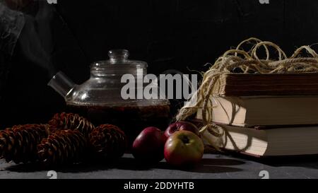 Glass teapot, old books, pine trees and apples on dark gray background. Stock Photo