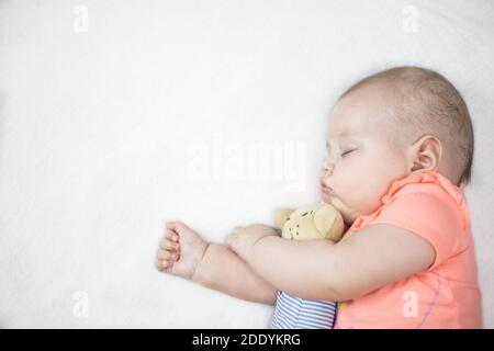 Newborn baby girl sleeping sweetly on a white bed with a toy teddy bear in her arms Stock Photo