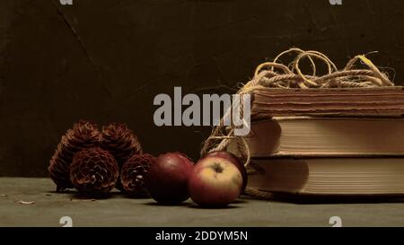 Old books with apples and pines on dark gray background. Vintage style picture. Books with yellow paper. Stock Photo