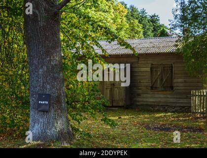 Mailbox, with word "Post" written on it, attached to a tree trunk with old wooden house on background. Stock Photo
