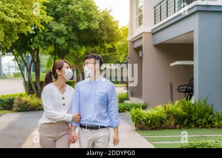 Asian couples with protective masks walking in pathway in public park at village together during the Coronavirus epidemic Stock Photo