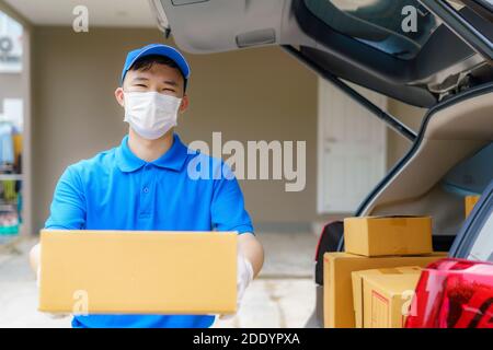 Asian Delivery man services courier working with cardboard boxes on van during the Coronavirus (COVID-19) pandemic, courier wearing medical mask and l Stock Photo