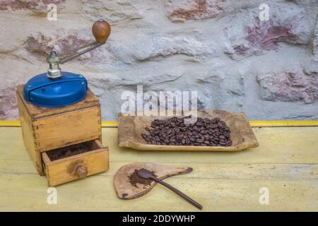 Vintage manual coffee grinder and coffee beans on old wooden table. Background - stone wall. Stock Photo