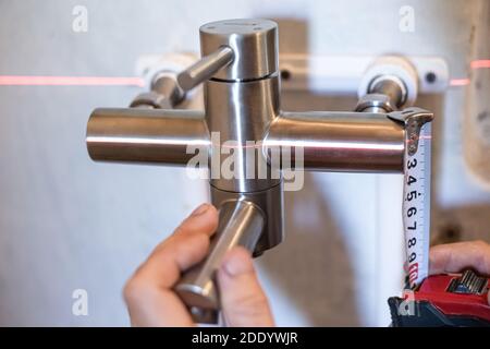 Sanhnik assembles an iron mixer for water supply, using a laser level and a tape measure. Plumbing installation and replacement. Stock Photo