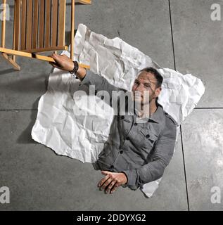 Man inside a photograph exits the photo by holding on to a chair. Stock Photo