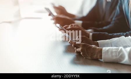 Lined up freelancers hands using smartphones testing app or updates sitting at the table. Blurred image. Selective focus on female hand in foreground Stock Photo