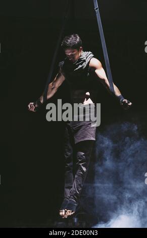 Acrobat shows his strength by spreading hands in difficult pul-up on the slings Stock Photo