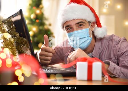 Man using a laptop at home with coronavirus mask with ok hand gesture on christmas holidays. Horizontal composition. Front view. Stock Photo
