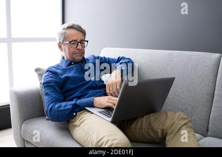 Man Using Laptop Sitting On Couch At Home Stock Photo