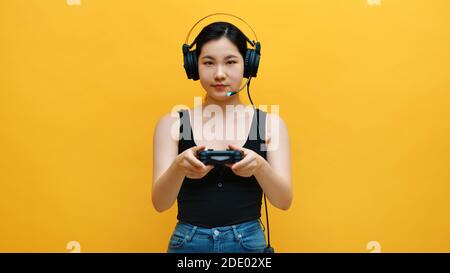 Focused young asian woman with headset and joystic controller playing video games. Isolated on yellow background. High quality photo Stock Photo