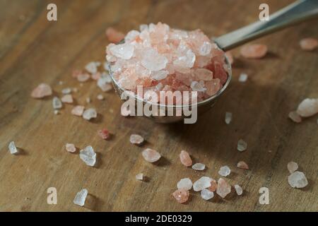 Close up of Himalayan pink rock salt in a silver measuring spoon on a wooden worktop. Stock Photo