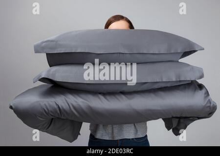 The woman is holding a warm duvet and gray feather pillows. Bedding for sleeping. Stock Photo