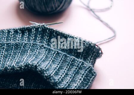 Knitting project underway. Knitting with a ball of aquamarine yarn and knitting needles on pink background. Woman knitting woolen clothes Stock Photo