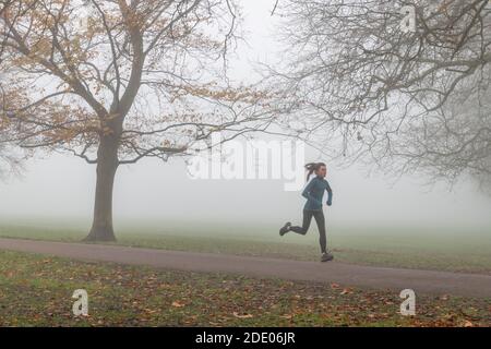 Cambridge, UK. 27th Nov, 2020. A morning jogger runs through thick fog on Jesus Green. Alan Copson/Alamy Live News Stock Photo