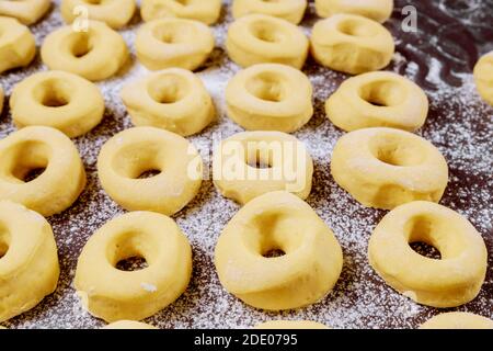 Close up of raw round sweet donuts on table with flour before frying. Stock Photo