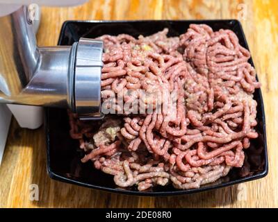 grinding of minced meat and onion in electric meat grinder close up on wooden table at home kitchen Stock Photo