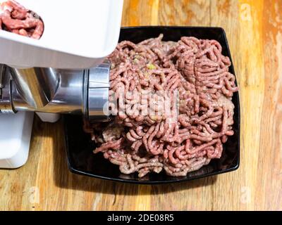 https://l450v.alamy.com/450v/2de08r5/side-view-of-grinding-of-minced-meat-and-onion-in-electric-meat-grinder-on-wooden-table-at-home-kitchen-2de08r5.jpg