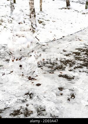 snowman from the first snow with fallen leaves on ice-covered path in frozen city park on cold autumn day Stock Photo