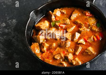 Close up view of stewed chicken livers with vegetables in tomato sauce in frying pan over dark stone background. Tasty dish for dinner. Stock Photo