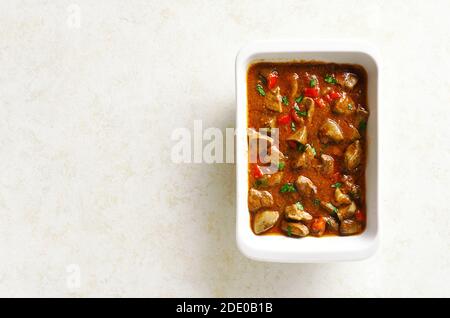 Stewed chicken livers with vegetables in baking dish over light stone background with free text space. Top view, flat lay Stock Photo