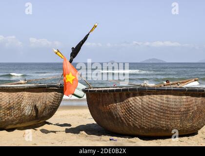 Close-up of basket boats on the sand in front of the sea. There is a Vietnam flag in one of them. An Bang Beach, Hoi An, Vietnam. Stock Photo