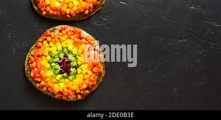 Rainbow veggie bell peppers pizza on black stone background with free text space. Vegetarian vegan or healthy food concept. Gluten free diet dish. Top Stock Photo
