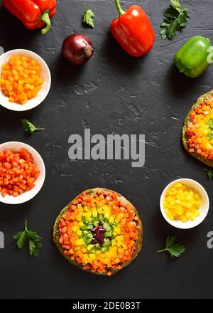 Frame of rainbow veggie bell peppers pizza and ingredients on black stone background with free text space. Vegetarian vegan or healthy food concept. G Stock Photo