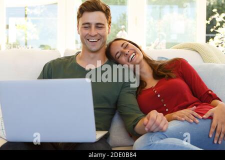 Caucasian couple sitting on a couch using laptop Stock Photo