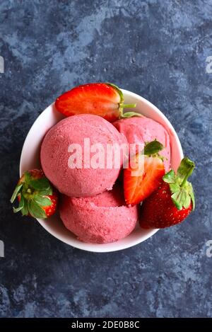 Strawberry ice cream scoop with fresh strawberries in bowl over blue stone background. Tasty summer cold dessert. Close up view Stock Photo