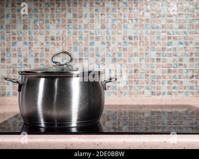 front view of closed used steel stockpot on black ceramic stove at home kitchen Stock Photo