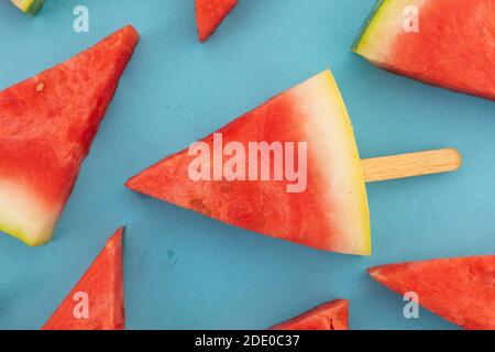 Close up of multiple watermelon triangles on wooden sticks on blue background Stock Photo
