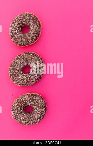 High angle view of three chocolate donuts with sprinkles on pink background Stock Photo