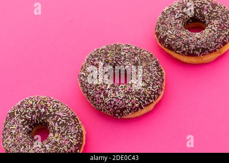 High angle view of three chocolate donuts with sprinkles on pink background Stock Photo