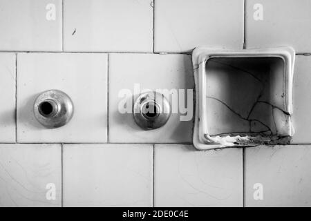 Black and white of bathroom detail. Tiled wall, broken ceramic soap dish and metal remnants of the tap. Interior of abandoned building in ruins. Stock Photo