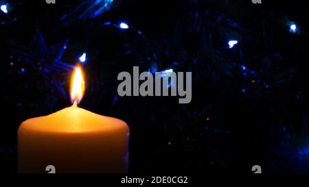 Blurred background. Burning candle. Orange candle light and blue garland lights. Night light picture. Stock Photo