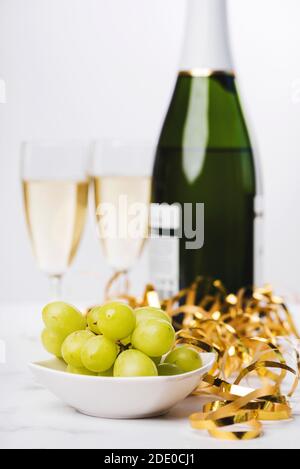 New Years Eve celebration concept background. Closeup of grapes with champagne bottle and two glasses blurred on the background on marble table. Sele Stock Photo